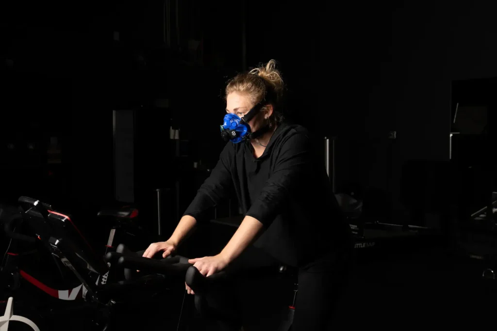 Athlete on an exercise bike in a dark gym wearing a SpiroFit metabolic analyzer mask
