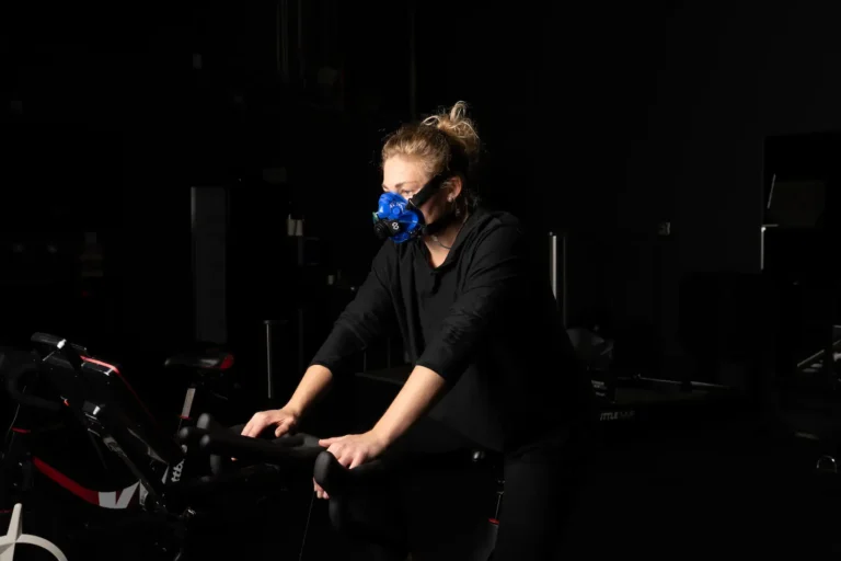 Athlete on an exercise bike in a dark gym wearing a SpiroFit metabolic analyzer mask